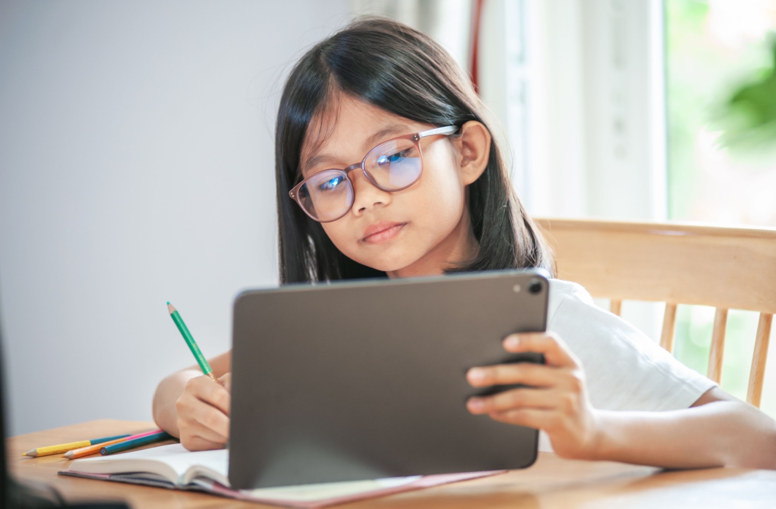 A small girl wearing glasses and looking into her ipad at a close distance