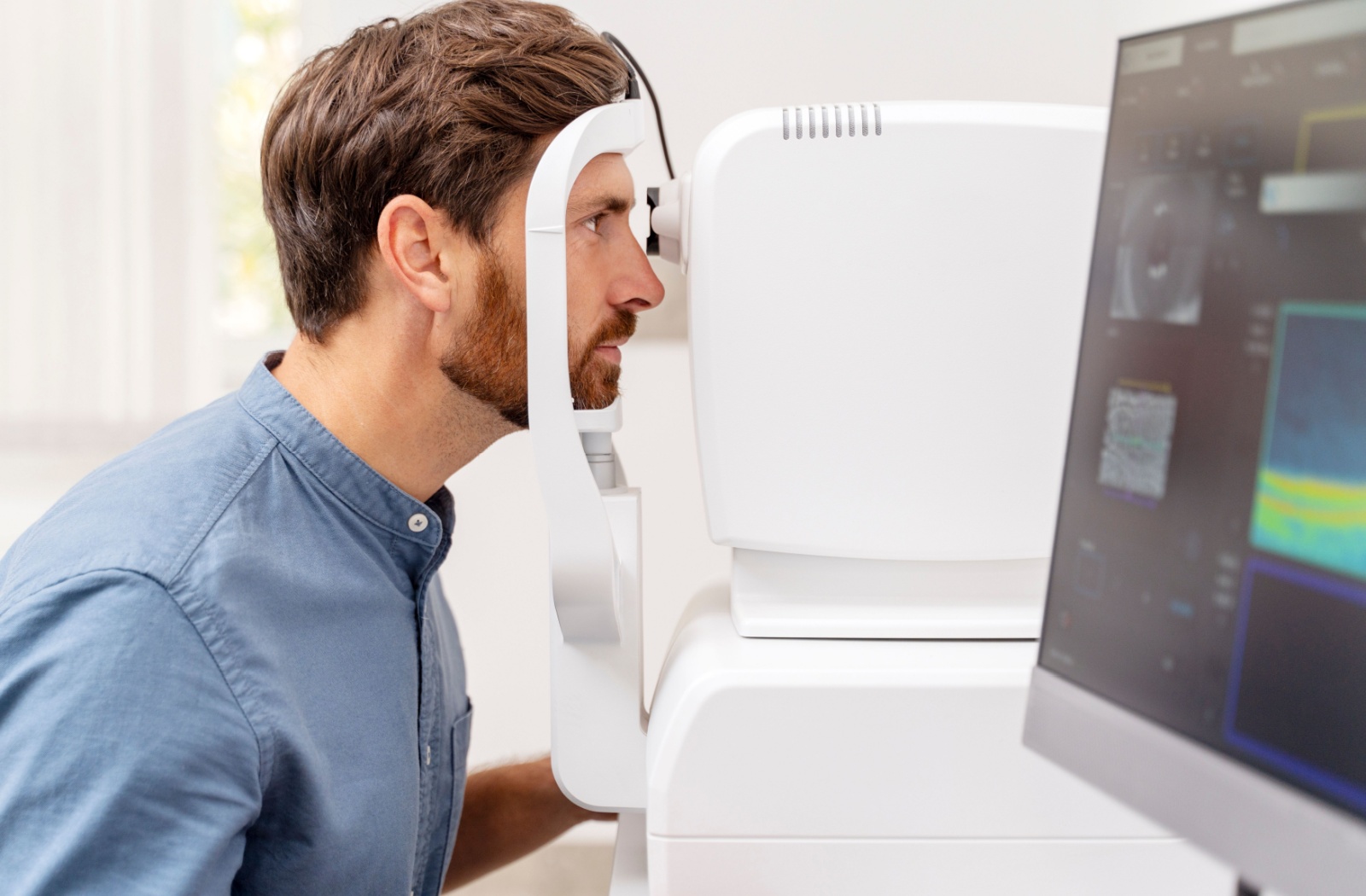 A man sitting with his face resting on the retinal imaging device with his left eye looking into the camera.