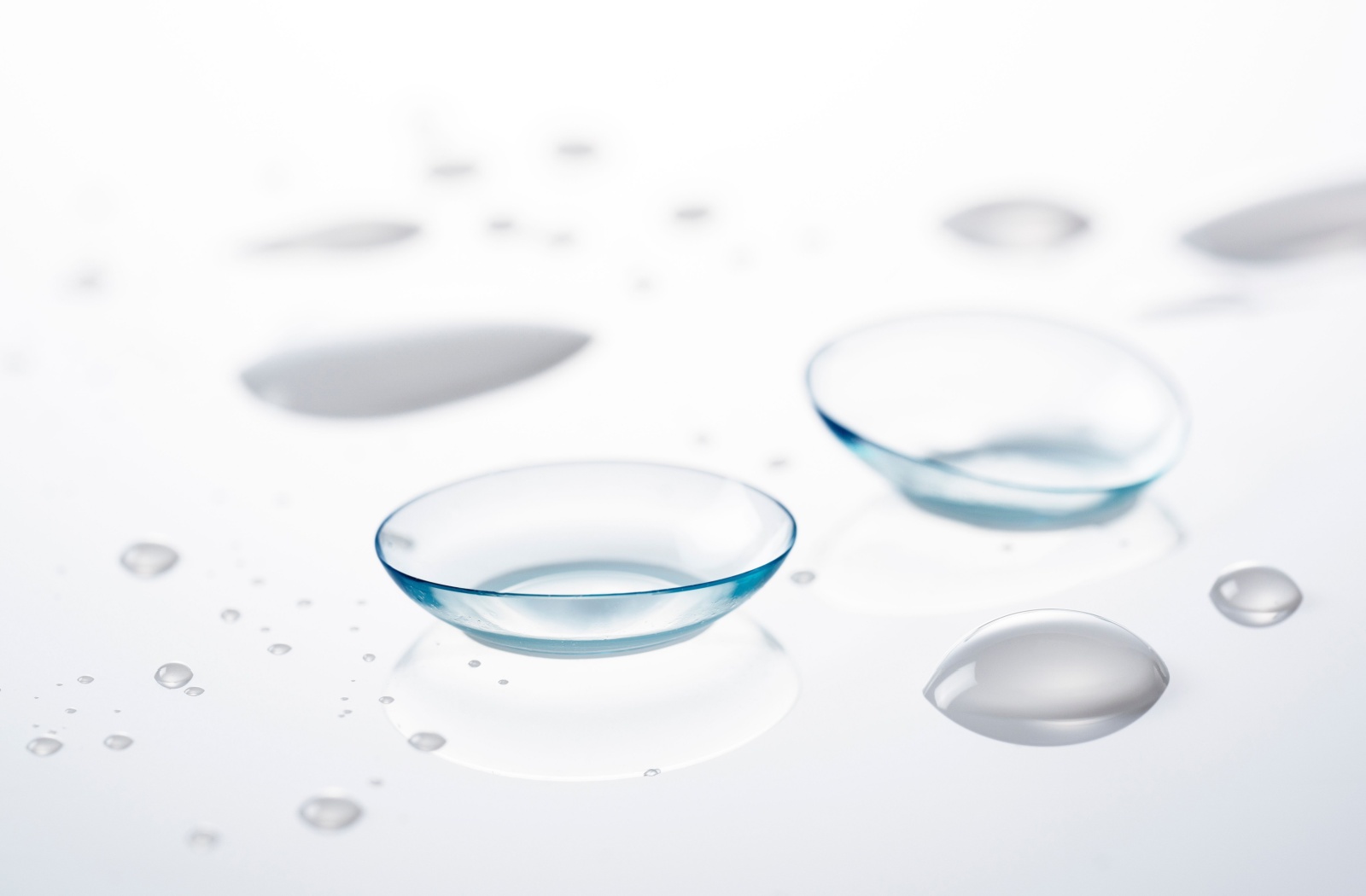 A pair of soft contact lenses sit on a glass surrounded by water droplets.