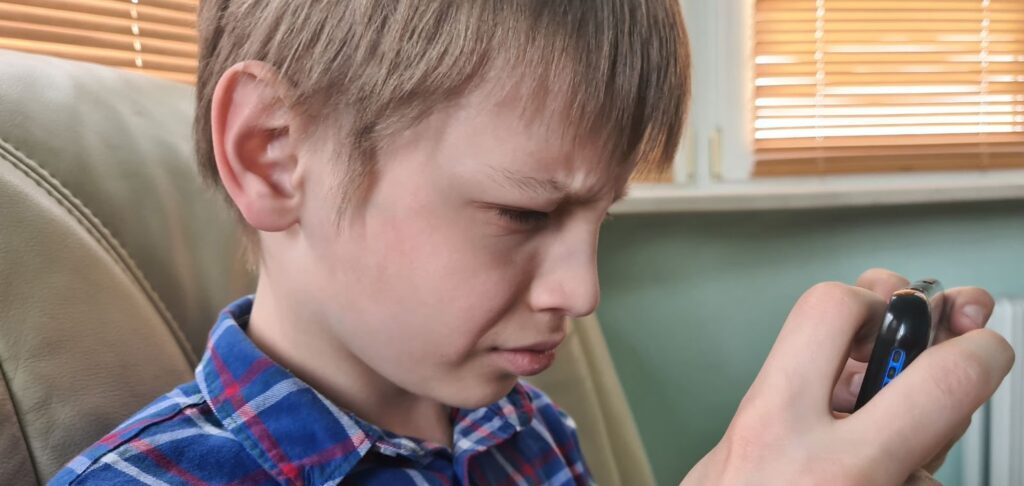 Child with poor eyesight squinting while looking at their phone screen.