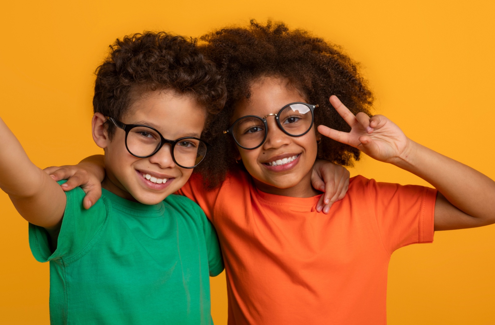 Two young smiling kids wearing eyeglasses, on a yellow background.